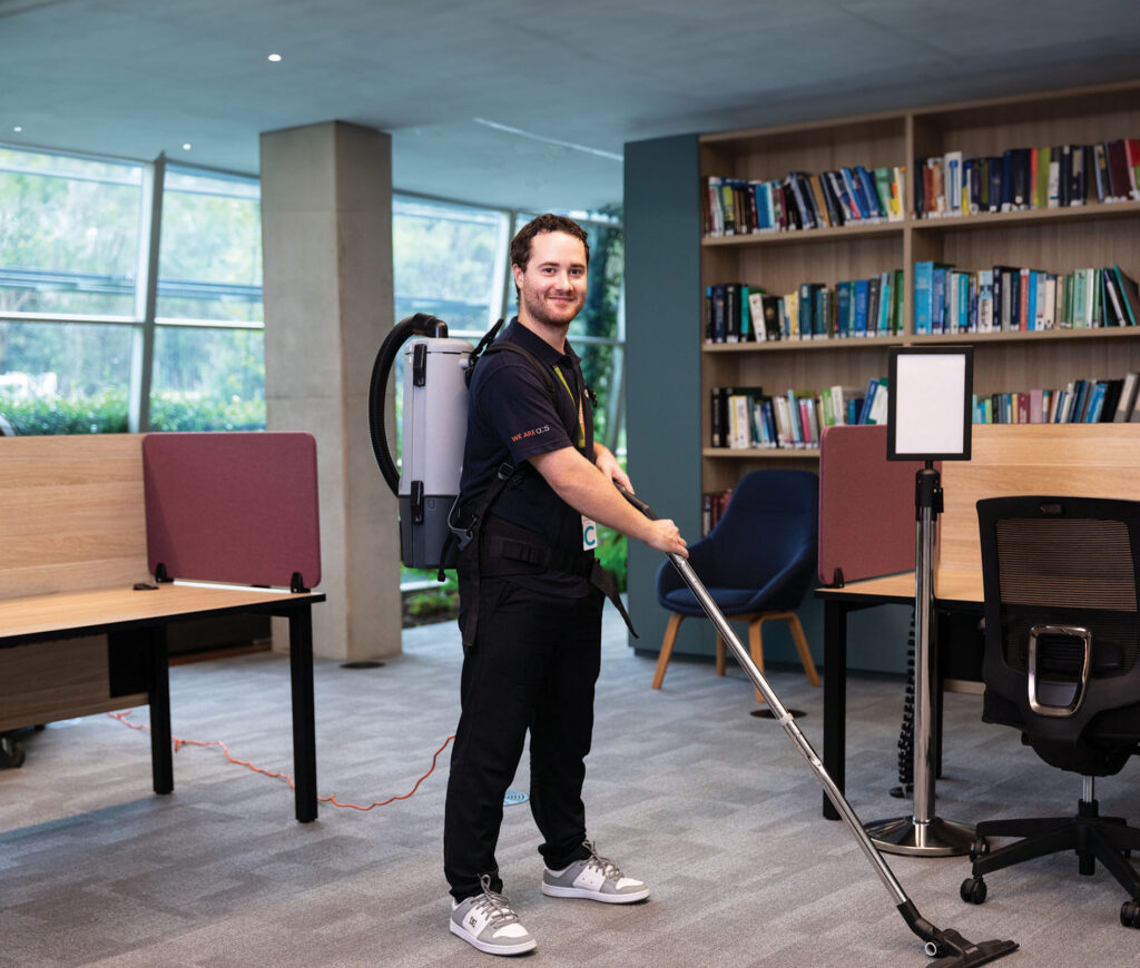 man cleaning a carpet using vacuum cleaner, smiling