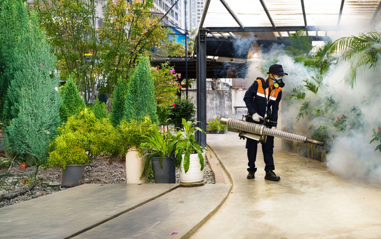 A man in a black jacket and hat sprays a large cloud of smoke, representing pest control efforts in Cambodia.