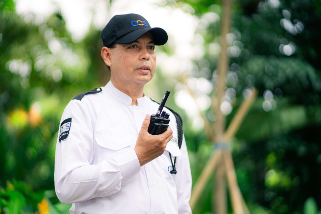 A security officer in a security uniform holds a walkie talkie, representing OCS Cambodia's commitment to safety.