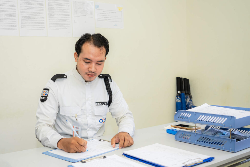 A man in a white shirt seated at a desk, representing a security officer in Cambodia.