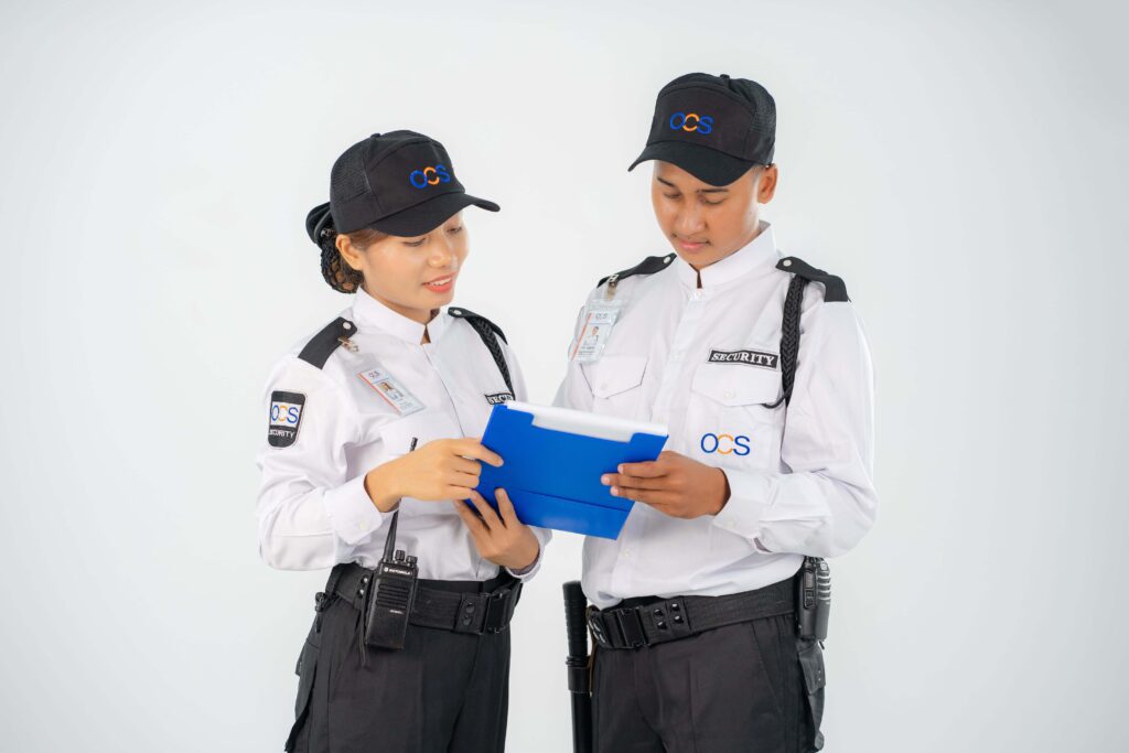 Two OCS Cambodia security officers stand side by side, each holding a blue folder, ready for duty.