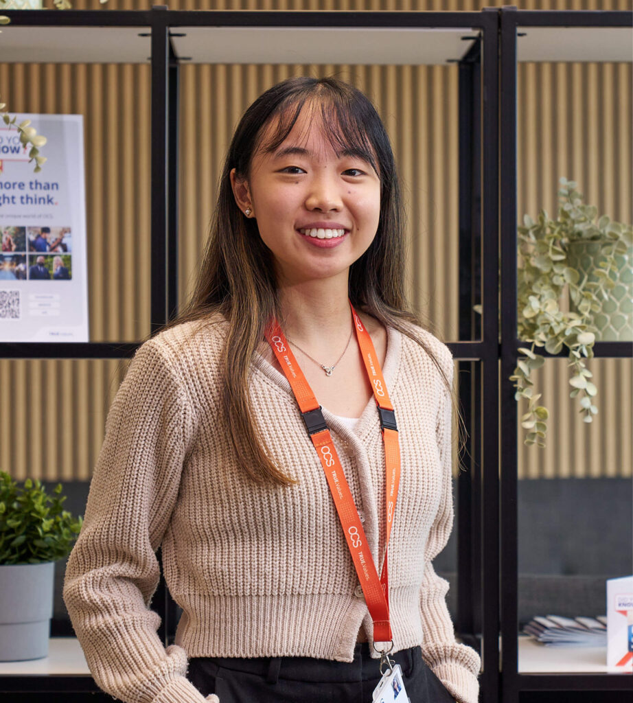 A young woman in a sweater stands confidently in front of a table, representing a new career journey at OCS.