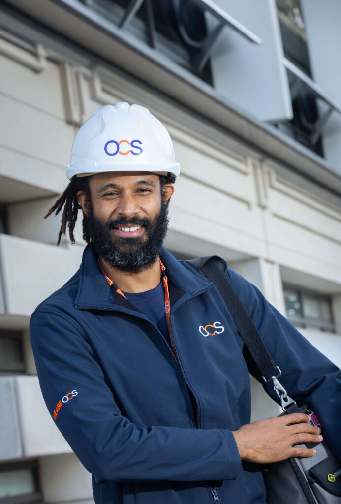 A bearded man wearing a hard hat, representing a colleague in hard services at OCS.