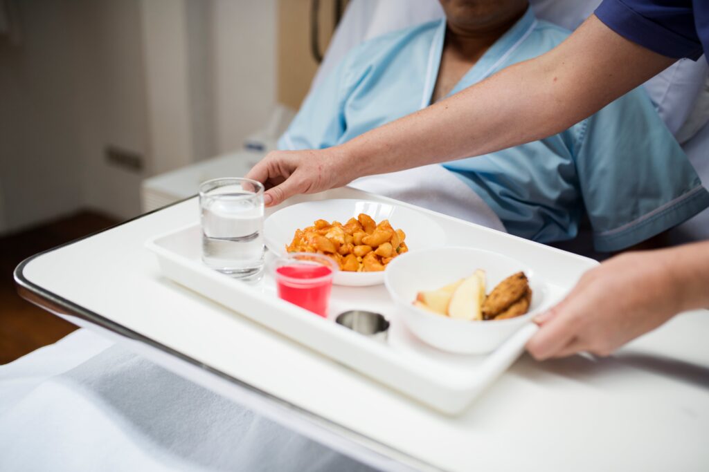 A nurse presents a tray filled with food and drinks, showcasing hospital catering services in a healthcare setting.