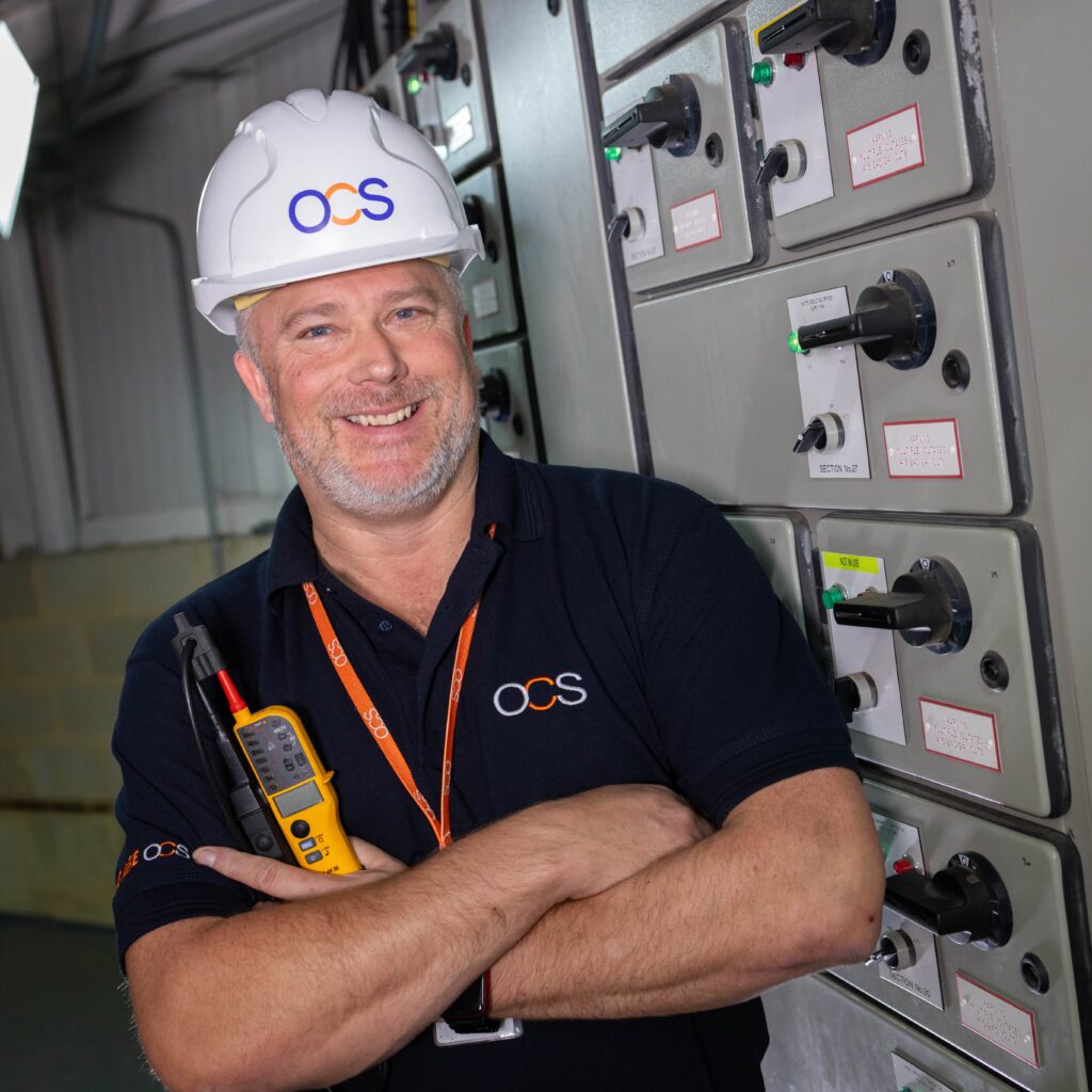 A man in a hard hat, representing an OCS hard services colleague, stands confidently at a construction site.