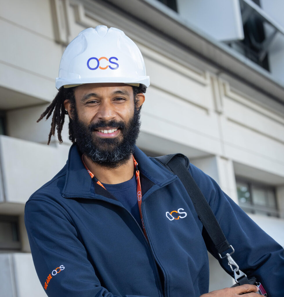 A bearded man wearing a hard hat, representing a colleague in hard services at OCS.