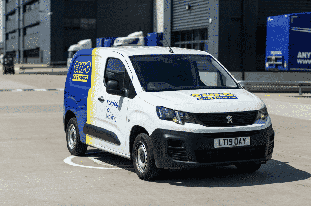 A white Peugeot van with Euro Car Parts logo and Keeping You Moving text is parked outdoors. The vans license plate reads LT19 OAY. Industrial buildings are visible in the background.