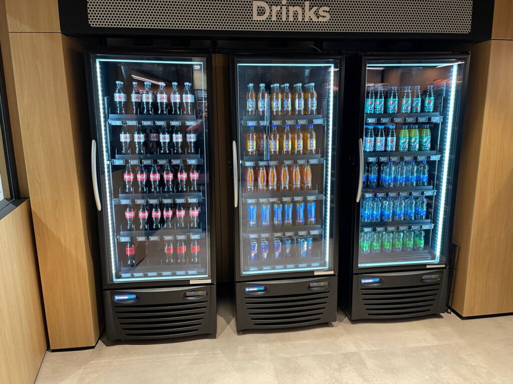 Three refrigerated display cases filled with various bottled drinks, including Coca-Cola, orange Fanta, Sprite, and Mountain Dew, organized neatly on shelves in a well-lit beverage section.