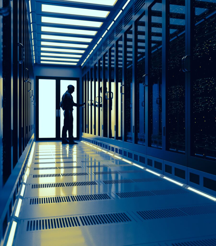 A person stands in a brightly lit, modern server room, surrounded by rows of tall server racks with glass doors. The floor and ceiling have geometric patterns and glowing lights.