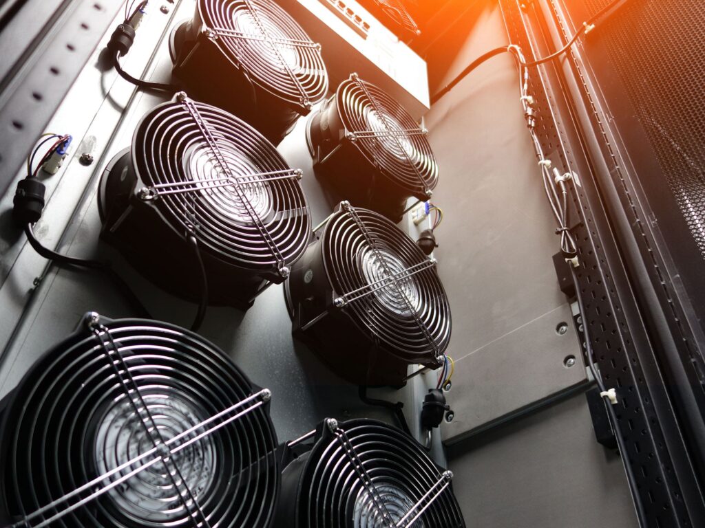 Close-up view of six cooling fans mounted vertically inside a server rack, with cables attached, used for cooling computer or mining equipment; orange light glows from the top corner.