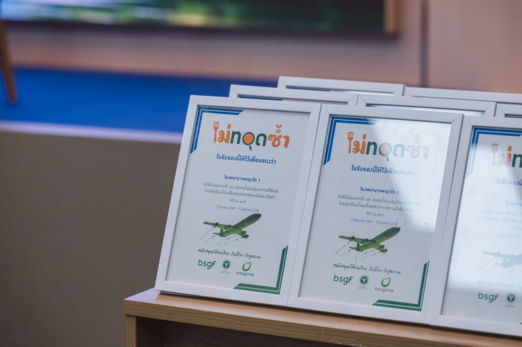 Several framed certificates with Thai text and illustrations of green airplanes are displayed standing upright on a wooden surface. The certificates have white borders and logos at the bottom.