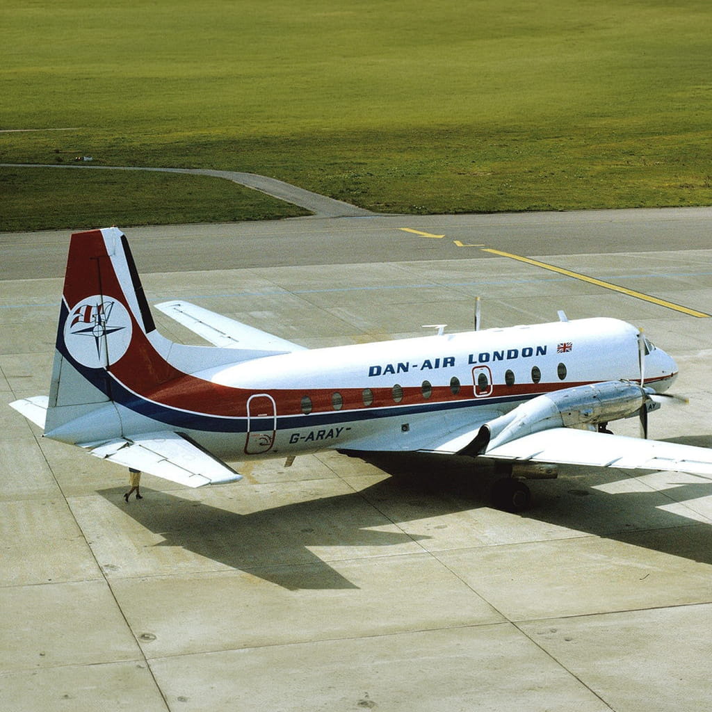 A Dan-Air London passenger aeroplane is parked on an airport apron with green grass in the background. The aircraft has a red, white, and blue livery and the registration G-ARAY is visible on the fuselage.