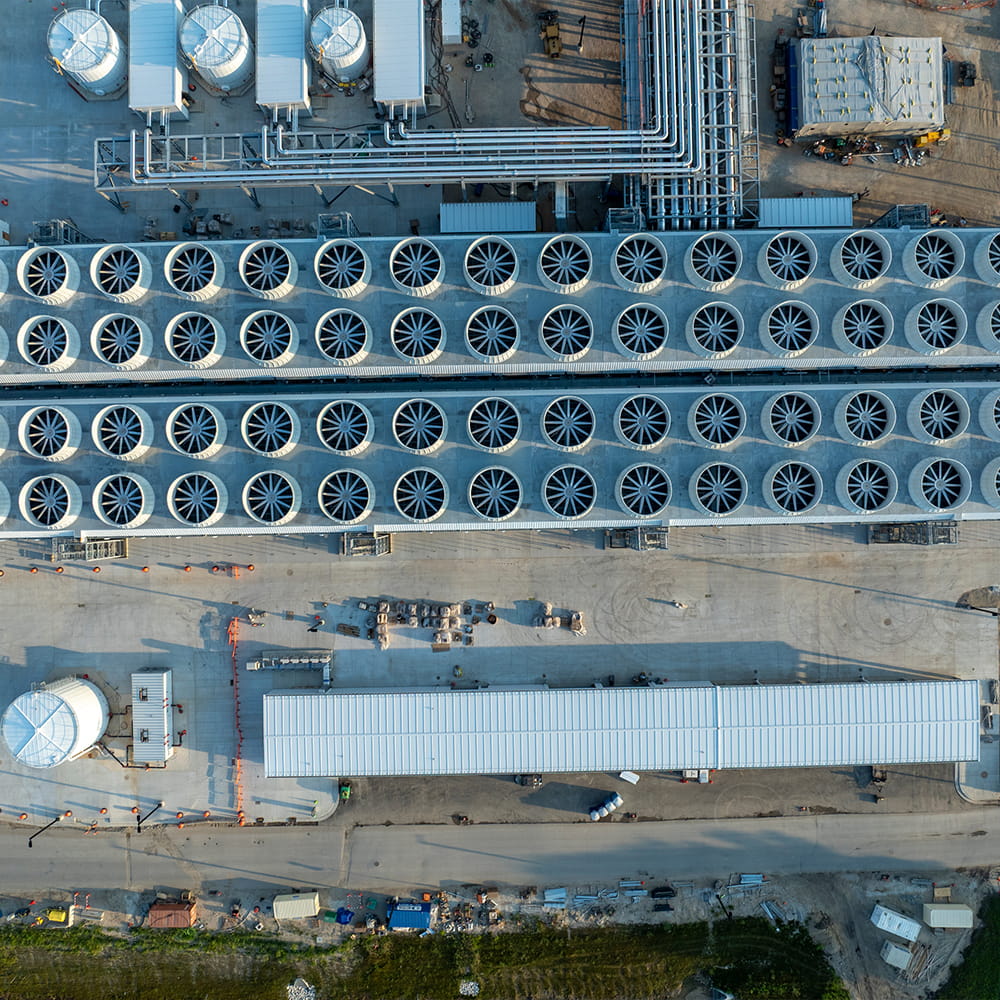 Aerial view of an industrial facility with rows of large fans, storage tanks, pipes, and buildings, possibly related to energy or data processing.