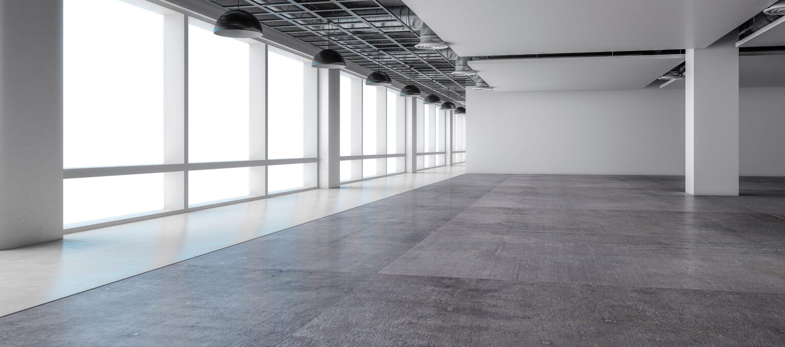 Empty modern office space with large floor-to-ceiling windows, white walls, exposed ceiling, and polished concrete floor. Natural light fills the room from the windows on the left side.