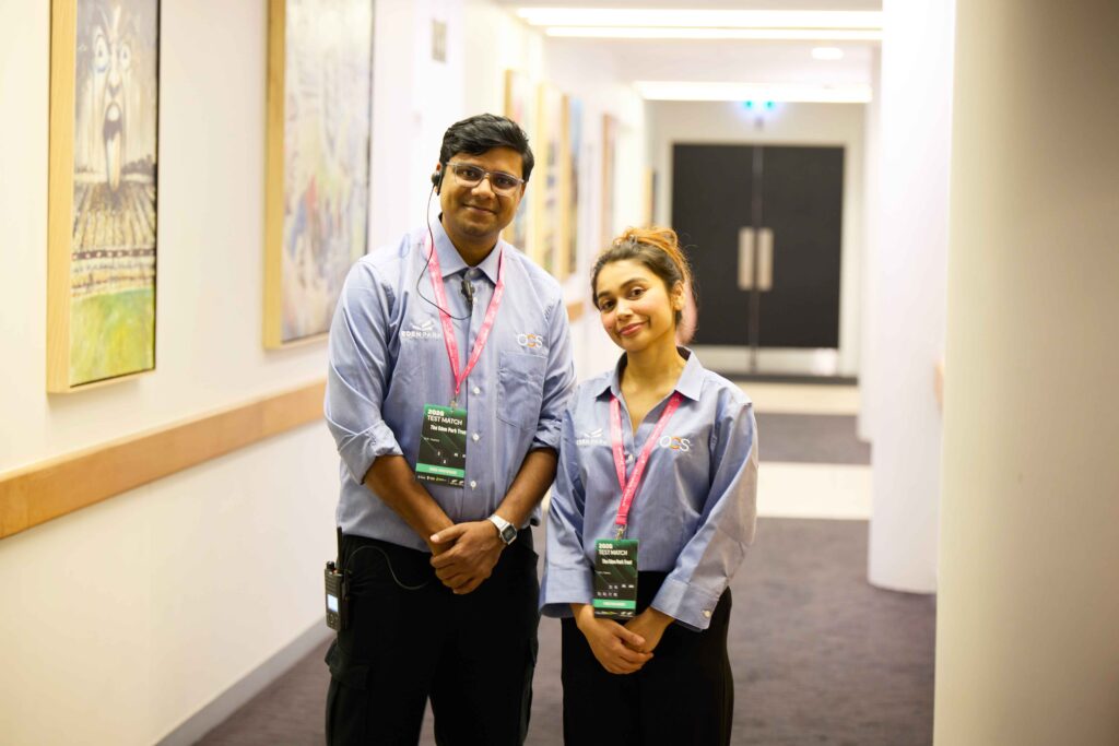 A man and a woman in matching blue staff shirts and lanyards standing in an office corridor.