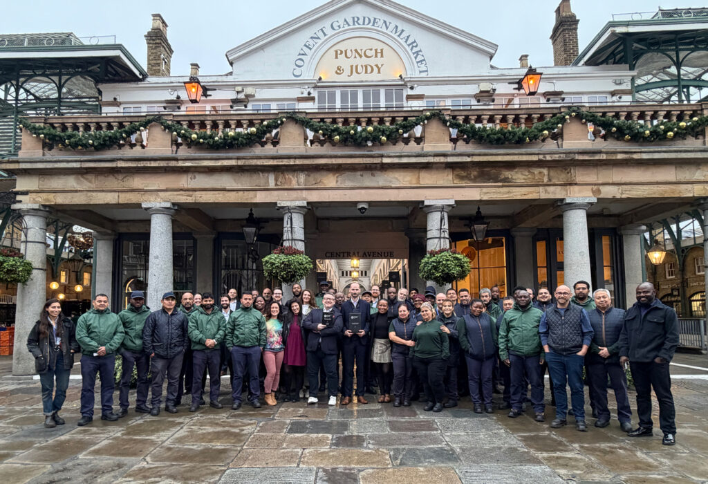 A large group of people posing for a photo in front of the Covent Garden Market building in London.