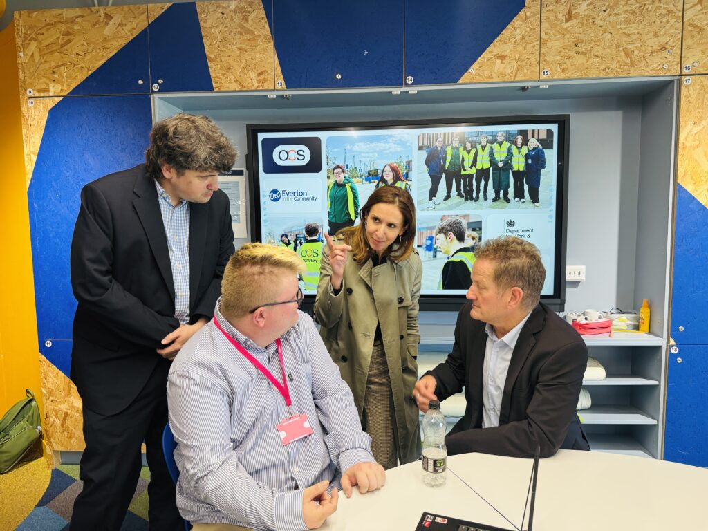 Four people gather around a table while looking at a large wall-mounted screen displaying photos of a community project.