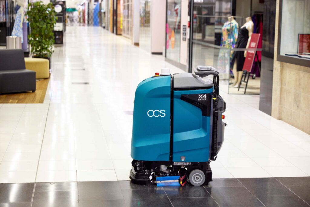 A teal OCS X4 ROVR floor cleaning machine standing in a shopping centre corridor.