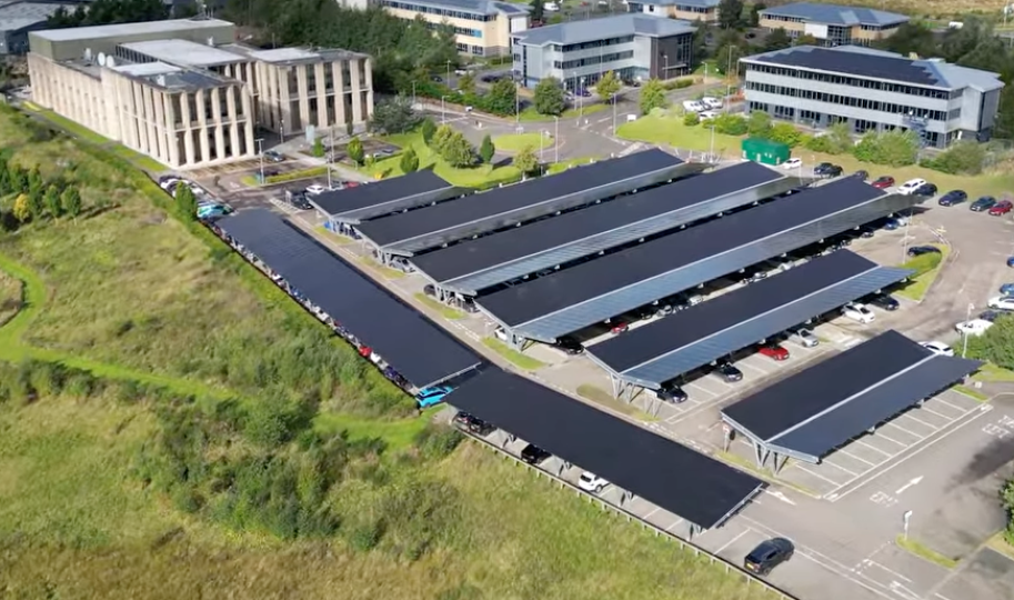 Aerial view of a parking lot featuring multiple rows of solar panel carports next to office buildings.