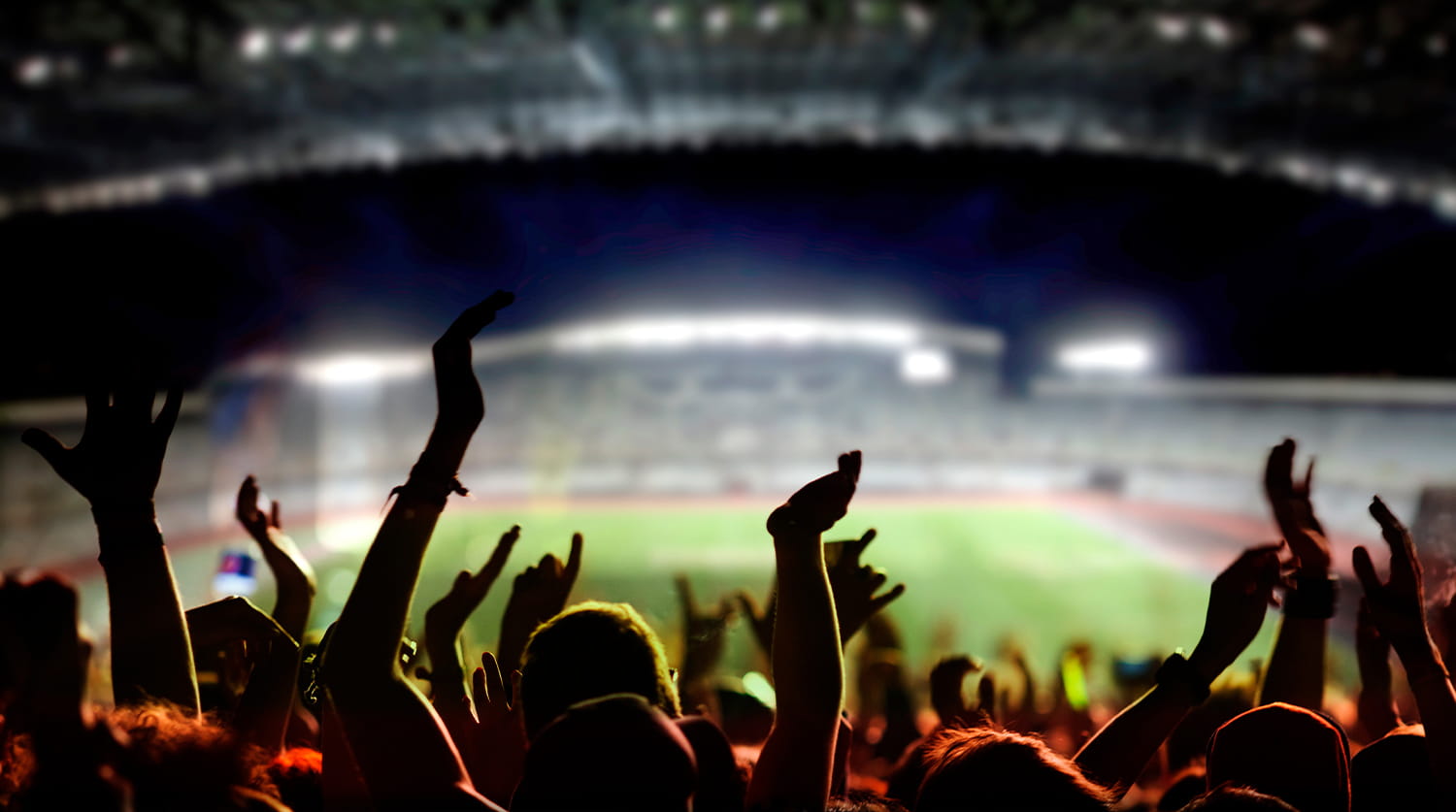 A crowd in a stadium cheering with their hands raised.